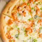 overhead of a Buffalo chicken pizza with one slice cut into, garnished with green onions