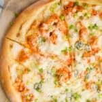overhead of a Buffalo chicken pizza with one slice cut into, garnished with green onions