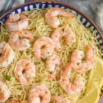 overhead view of a bowl of shrimp scampi garnished with lemon wedges, parsley, and parmesan cheese