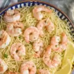 overhead view of a bowl of shrimp scampi garnished with lemon wedges, parsley, and parmesan cheese