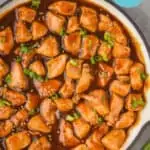 overhead view of sticky chicken in a skillet garnished with sesame seeds and green onion