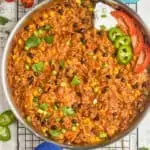 overhead view of a skillet full of cheesy taco casserole recipe garnished with cilantro, scallions, sour cream, jalapeños, and tomatoes