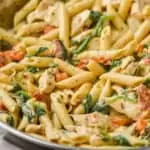 side view of a pan of creamy tuscan chicken pasta in a skillet with tomatoes and toasted garlic bread in the background