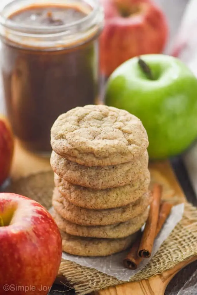 a stack of apple butter cookies with a jar of apple butter and an apple in the background