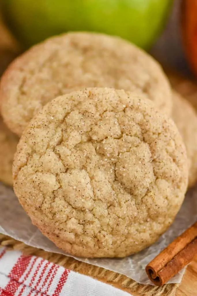 a close up view of an apple cookie on parchment paper with a cinnamon stick next to it