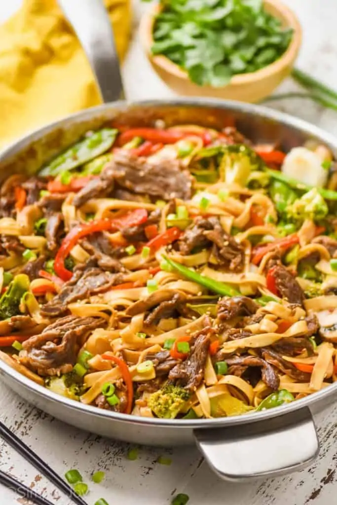 skillet of beef lo mein garnished with scallions and sesame seeds