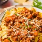 a plate of pappardelle bolognese sauce garnished with freshly grated parmesan and parsley