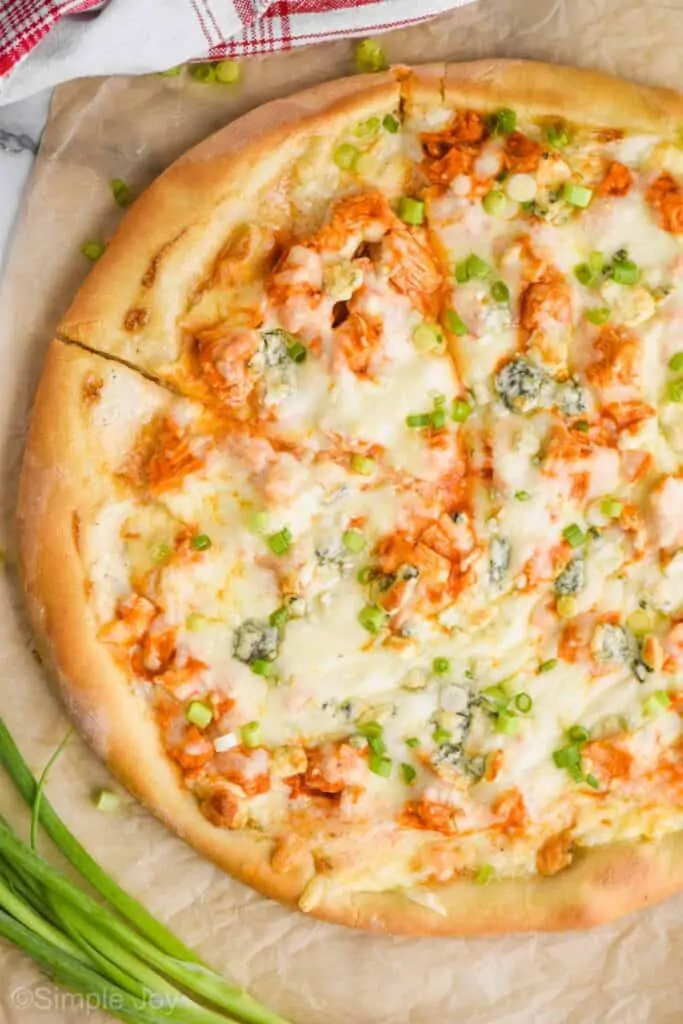 overhead of a Buffalo chicken pizza with one slice cut into, garnished with green onions