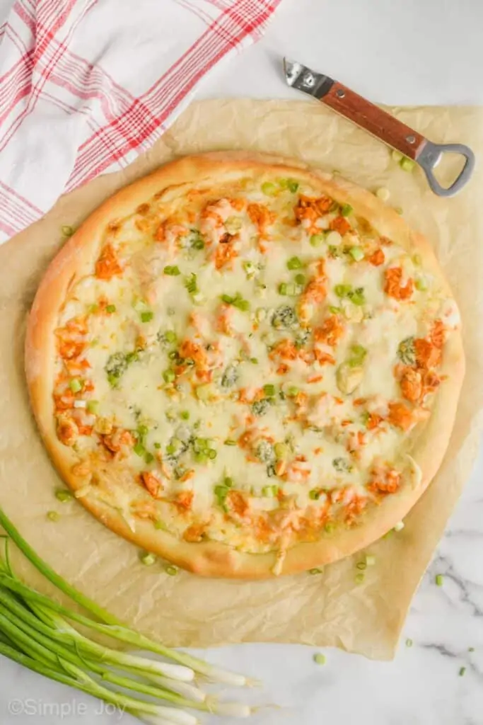 overhead of an entire buffalo chicken pizza next to some green onions and a bottle opener