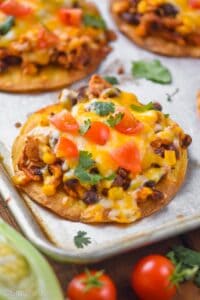 shredded chicken tostada on a rimmed baking sheet garnished with diced tomatoes and cilantro