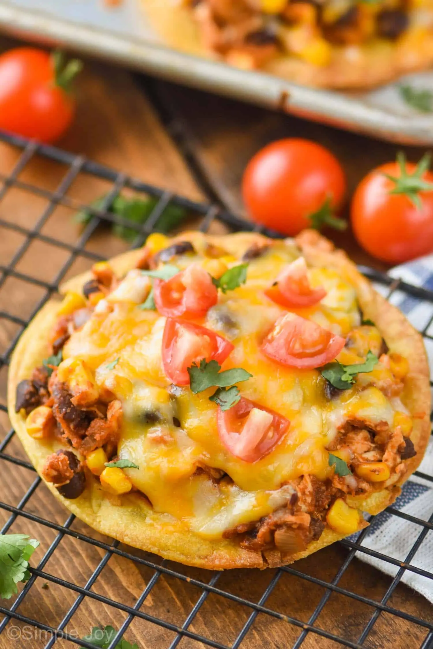 close up of a chicken tostada recipe on a wire cooling rack with diced tomatoes and fresh cilantro