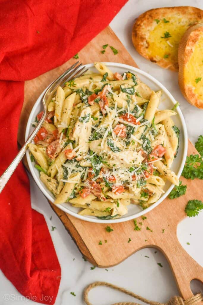 overhead view of a plate of tuscan chicken pasta garnished with parsley and parmesan cheese, with two pieces of garlic bread off to the side