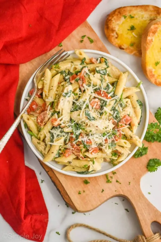 overhead view of a plate of tuscan chicken pasta garnished with parsley and parmesan cheese, with two pieces of garlic bread off to the side