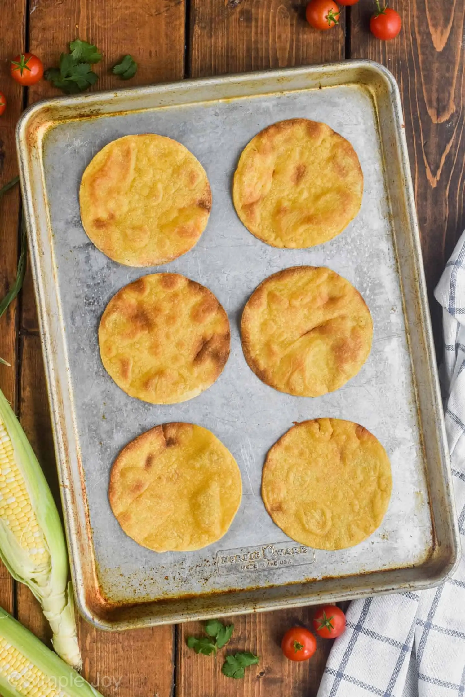 overhead photo of a rimmed baking sheet with six corn tortillas that have been baked to make homemade tostadas