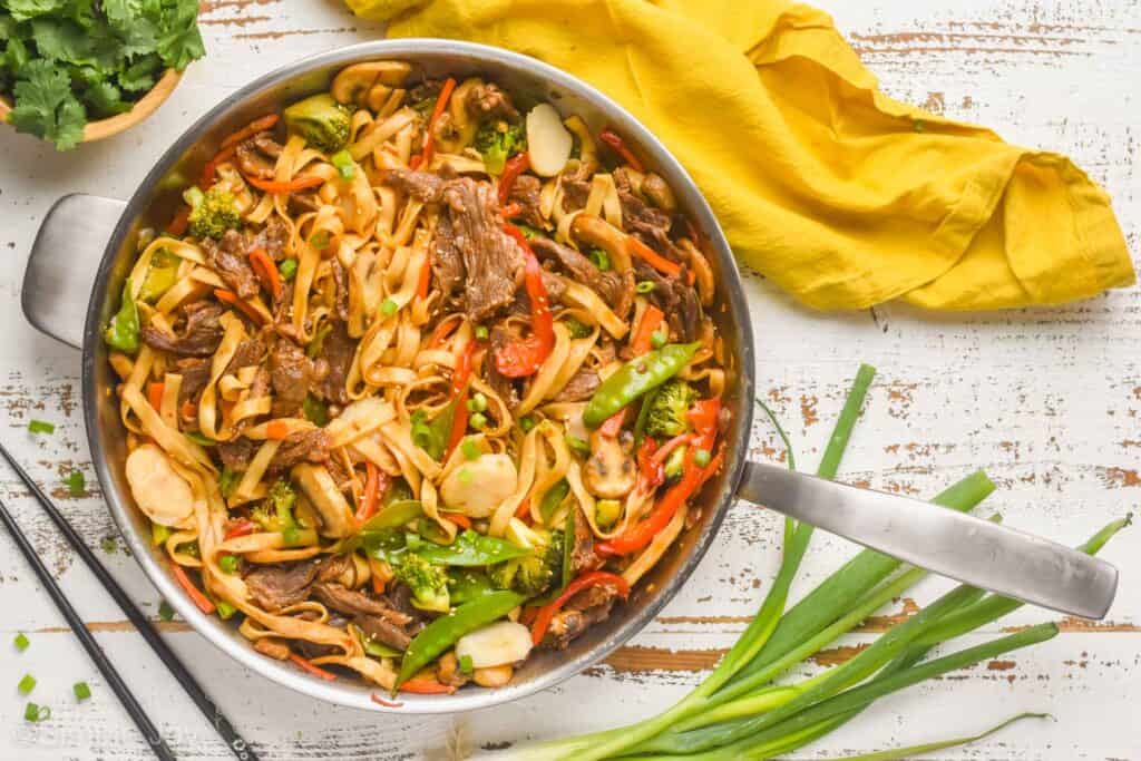 overhead of a skillet full of lo mein with scallions and cilantro around it