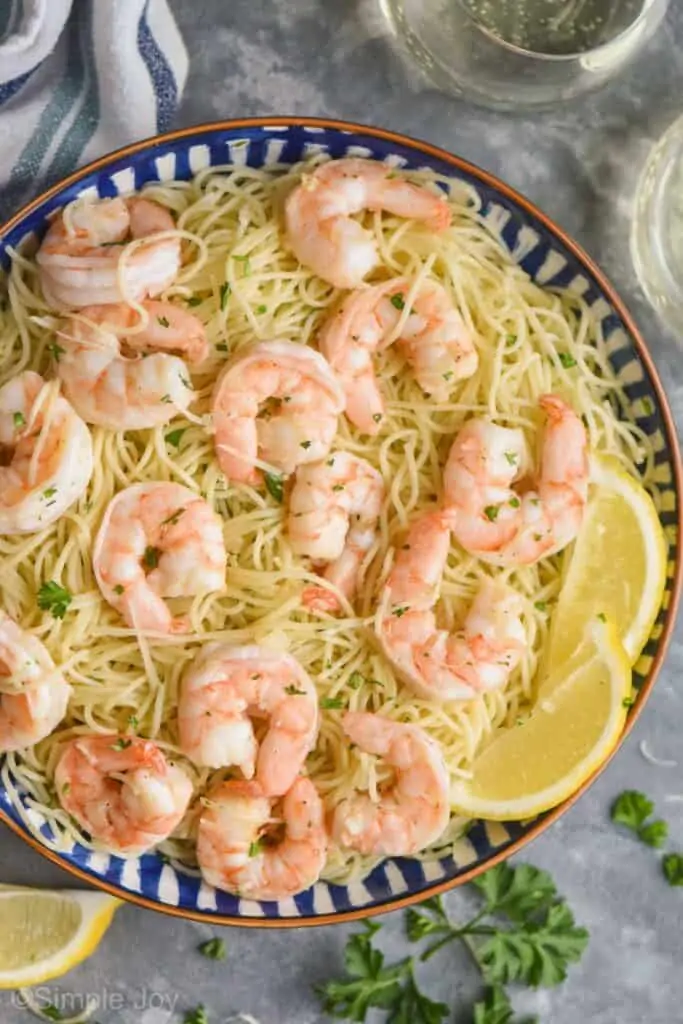 overhead view of a bowl of shrimp scampi garnished with lemon wedges, parsley, and parmesan cheese