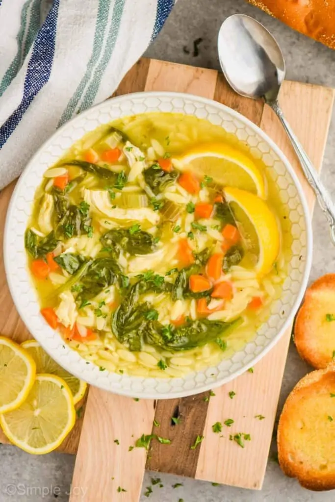 overhead of a bowl of lemon chicken orzo soup garnished with fresh parsley and two lemon wedges