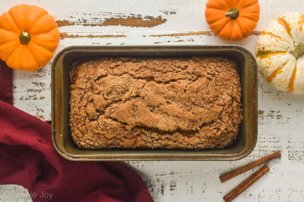 overhead view of pumpkin bread in a bread pan with cinnamon sticks and pumpkins around it