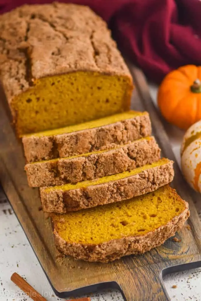 pumpkin bread topped with cinnamon sugar, sliced on a cutting board with small pumpkins around it