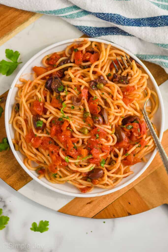 overhead of a small white plate with spaghetti alla puttanesca garnish with fresh parsley