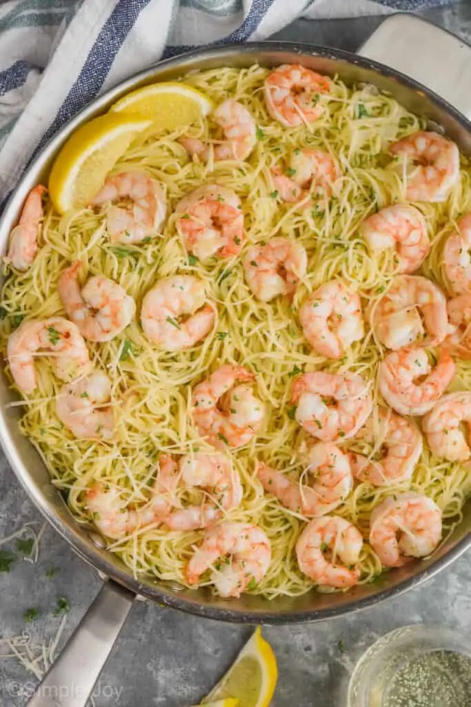 overhead view of a skillet full of shrimp scampi topped with fresh parsley and freshly grated Parmesan cheese and garnished with lemon wedges