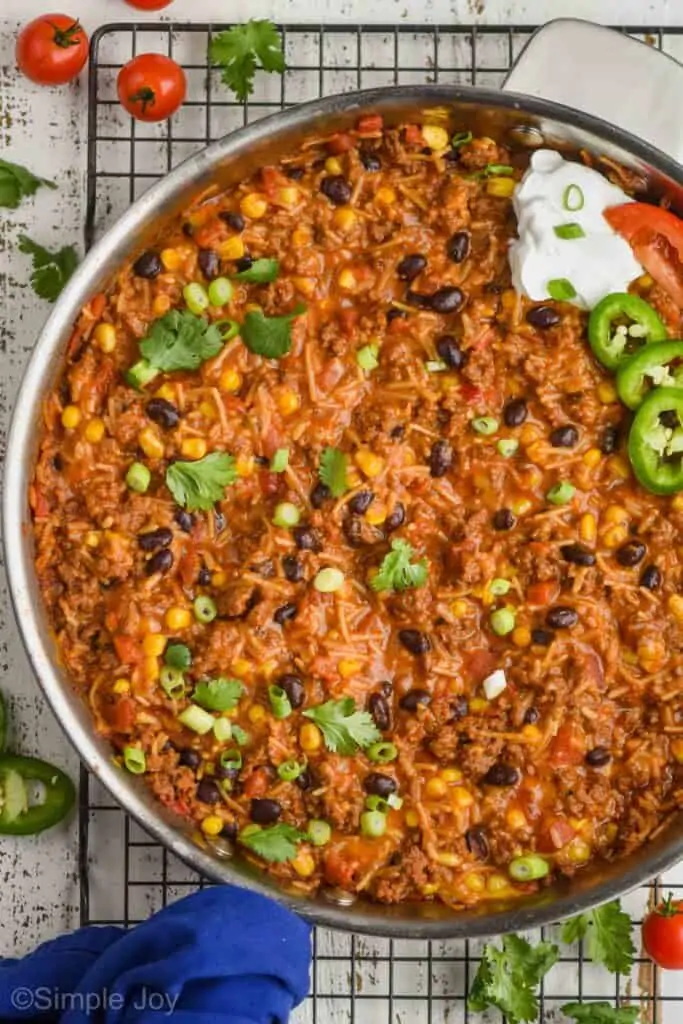 overhead view of a skillet full of cheesy taco casserole recipe garnished with cilantro, scallions, sour cream, jalapeños, and tomatoes