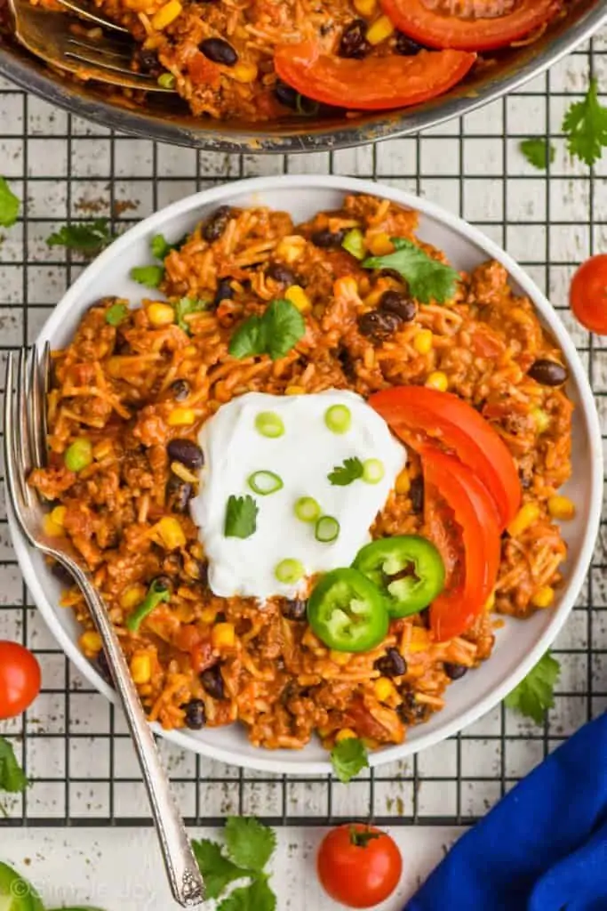 overhead view of a small white plate with taco casserole, sour cream, scallions, tomato slices, and jalapeño slices