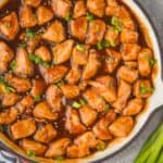 overhead view of sticky chicken in a skillet garnished with sesame seeds and green onion