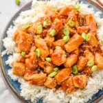 overhead of sticky chicken on a bed of rice, garnished with scallions and sesame seeds
