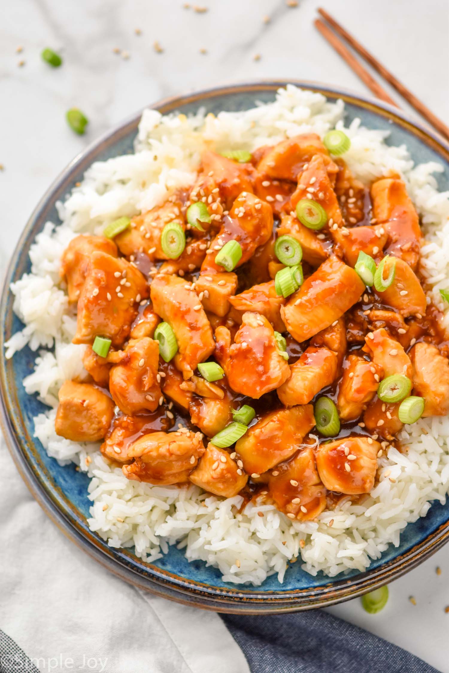 overhead of sticky chicken on a bed of rice, garnished with scallions and sesame seeds