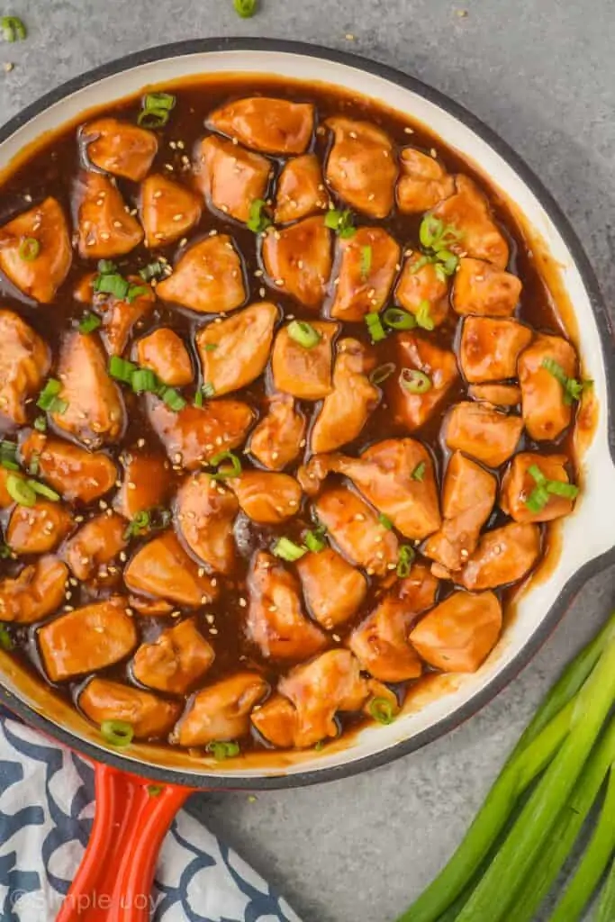 overhead view of sticky chicken in a skillet garnished with sesame seeds and green onion