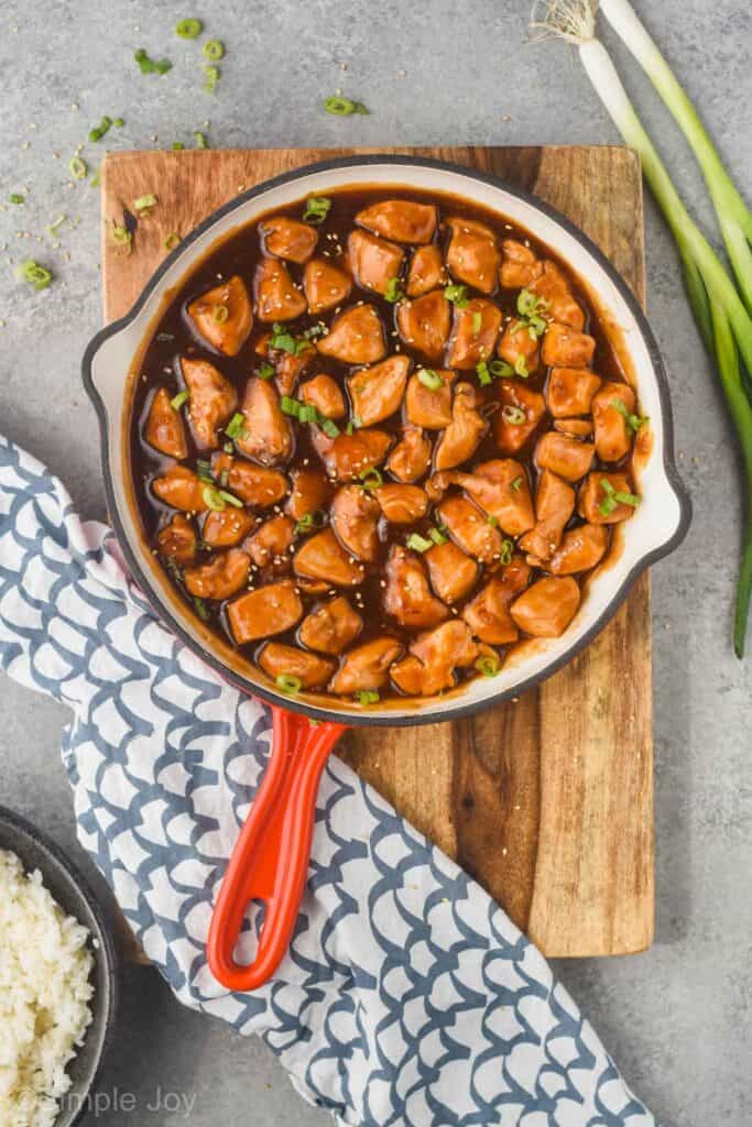 overhead view of a skillet holding sticky chicken recipe garnished with sesame seeds and sliced green onion
