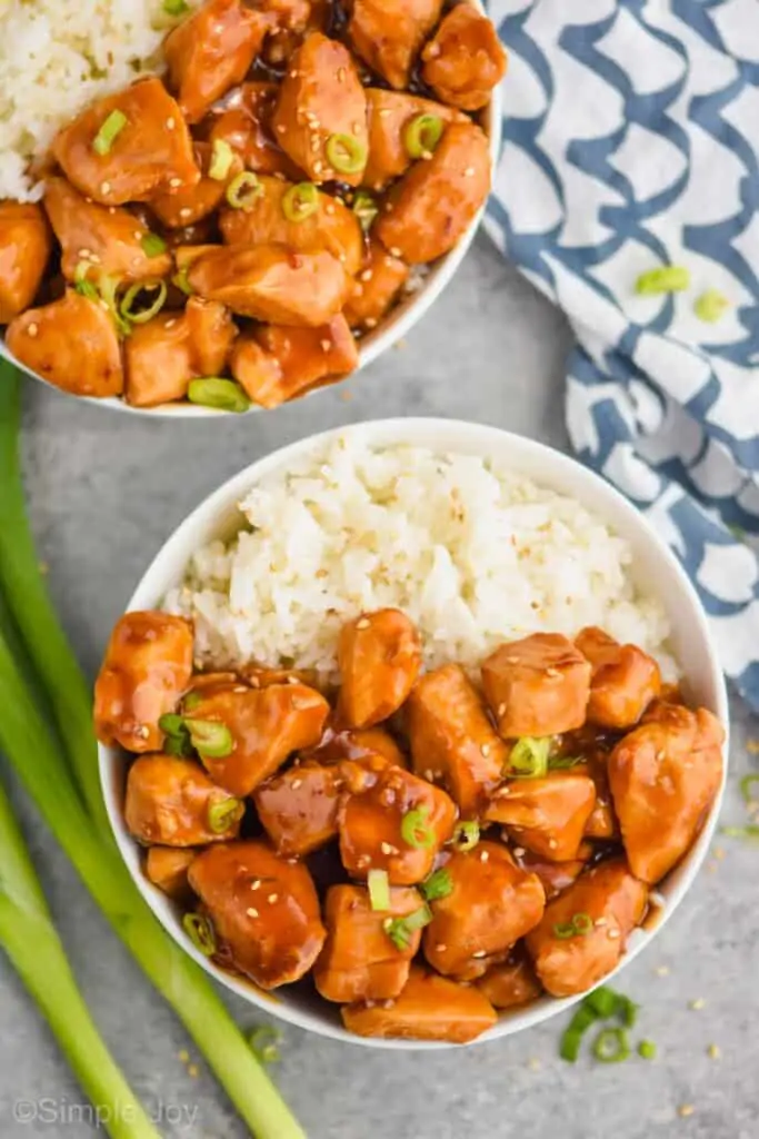 overhead view of a bowl of sticky chicken recipe with rice, garnished with sesame seeds and green onions