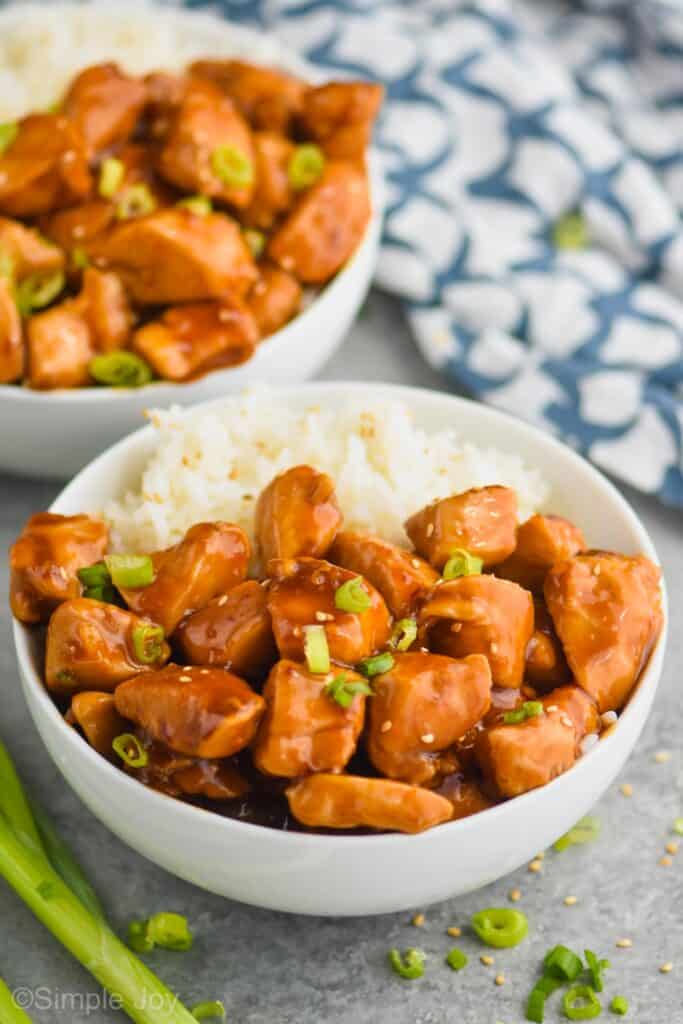 sticky chicken in a bowl with rice garnished with sesame seeds and green onions