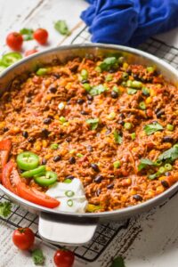 side view of a taco casserole in a skillet garnished with scallions, cilantro, and sour cream