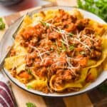 a plate of pappardelle bolognese sauce garnished with freshly grated parmesan and parsley