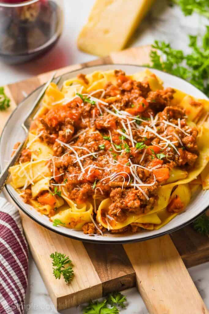 a plate of pappardelle bolognese sauce garnished with freshly grated parmesan and parsley