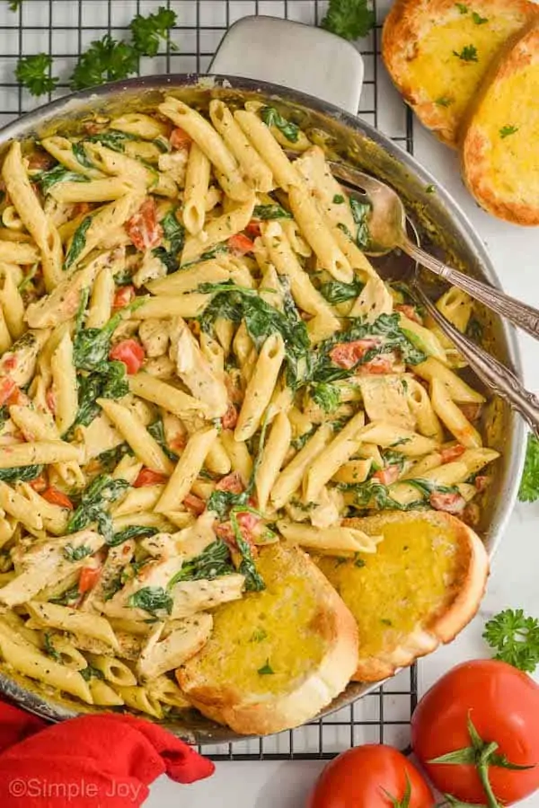 overhead view of a skillet with tuscan chicken pasta, and two slices of toasted garlic bread sticking into the pan