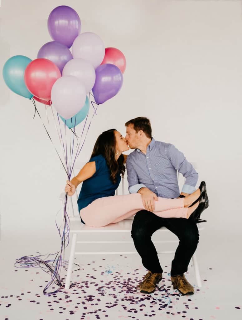 man kissing a woman on a bench, she's holding a bouquet of balloons