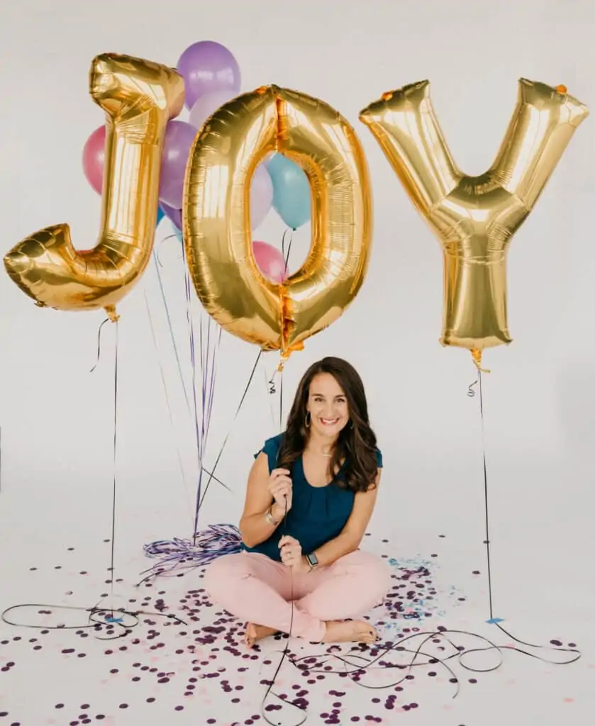 woman sitting cross legged on the floor holding balloons that spell out JOY