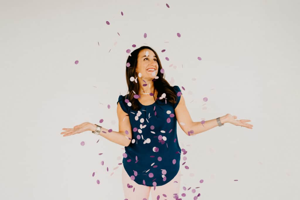woman standing under a shower of pink and purple confetti with her arms out