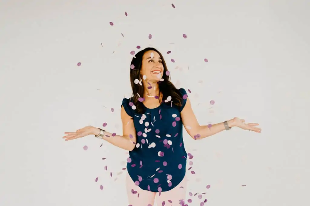 woman standing under a shower of pink and purple confetti with her arms out