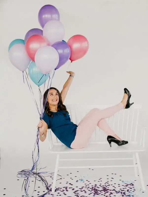 woman sitting on a bench with her feet in the air, holding a bouquet of balloons against a white background