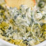 a bagel chip dipping into spinach and artichoke dip