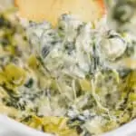 a bagel chip dipping into spinach and artichoke dip