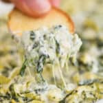 a bagel chip dipping into spinach and artichoke dip