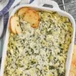 overhehead view of baked spinach artichoke dip in a white casserole dish surrounded by bagel chips