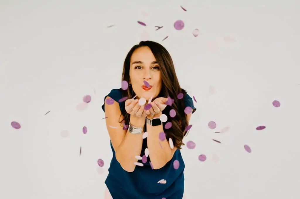 a woman blowing pink and purple confetti at the camera