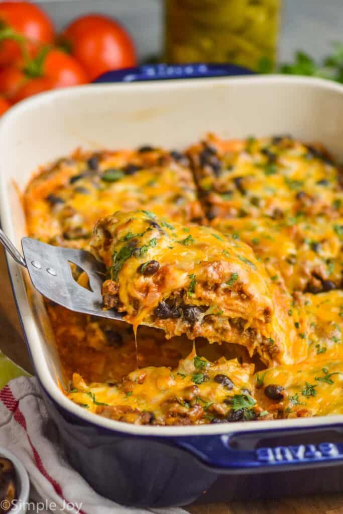 piece of cheese enchilada casserole being lifted out of baking dish