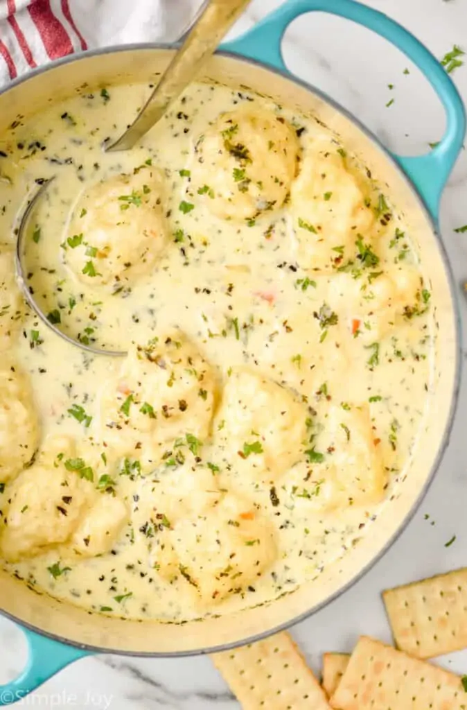 overhead view of a teal stockpot full of chicken and dumplings recipe, with crackers on the counter and fresh parsley on the cup